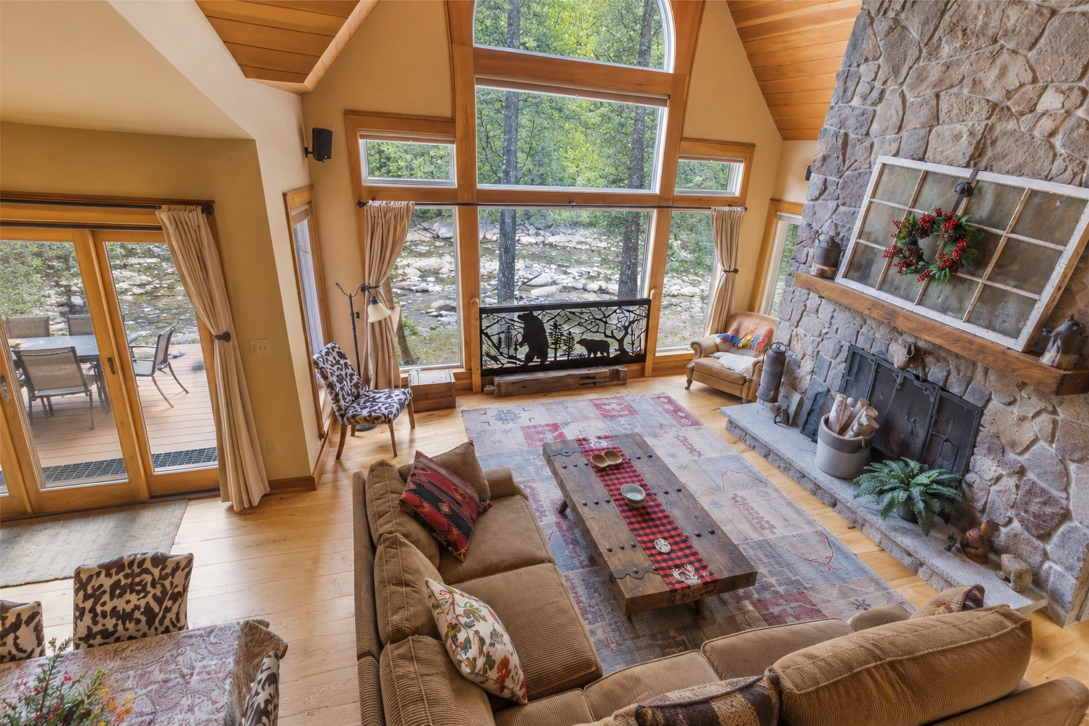 Sunroom addition with tall wood-framed windows, a stone fireplace, and a living area overlooking a rocky stream.